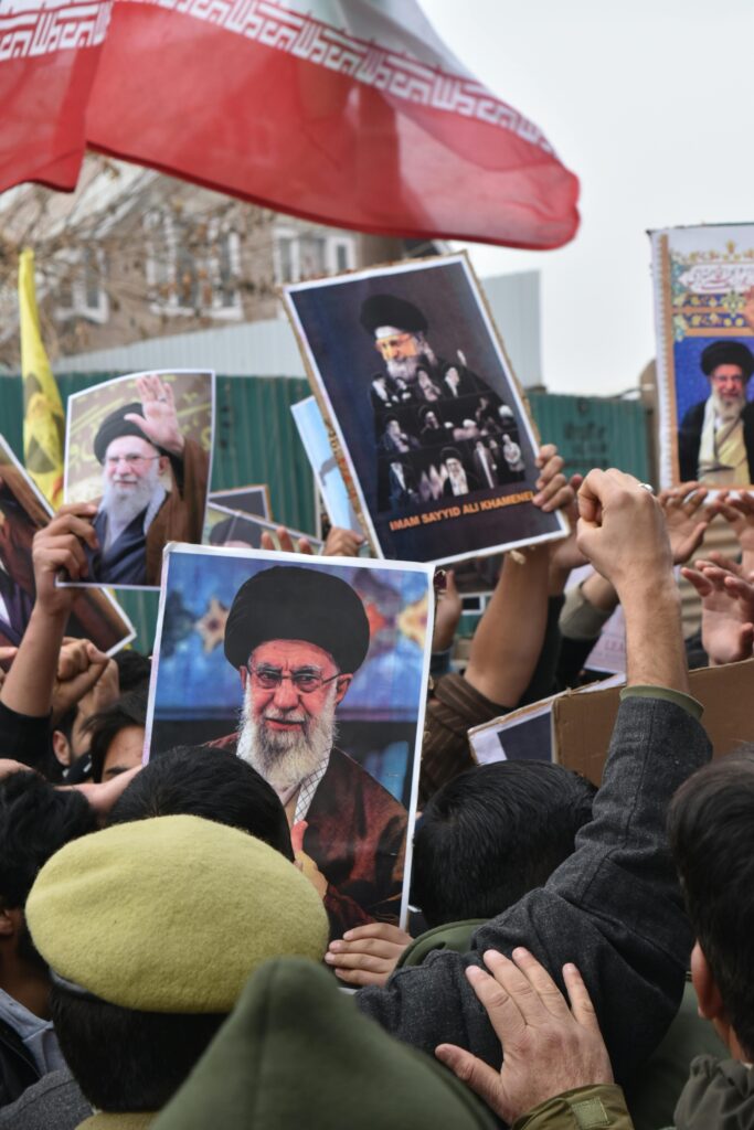 Protest scene featuring people holding posters of Iranian leaders with national flags visible.